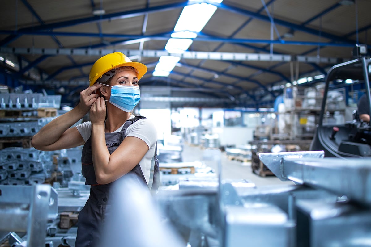 shot-of-female-factory-worker-in-uniform-and-hardhat-putting-on-face-mask-in-industrial-production-plant